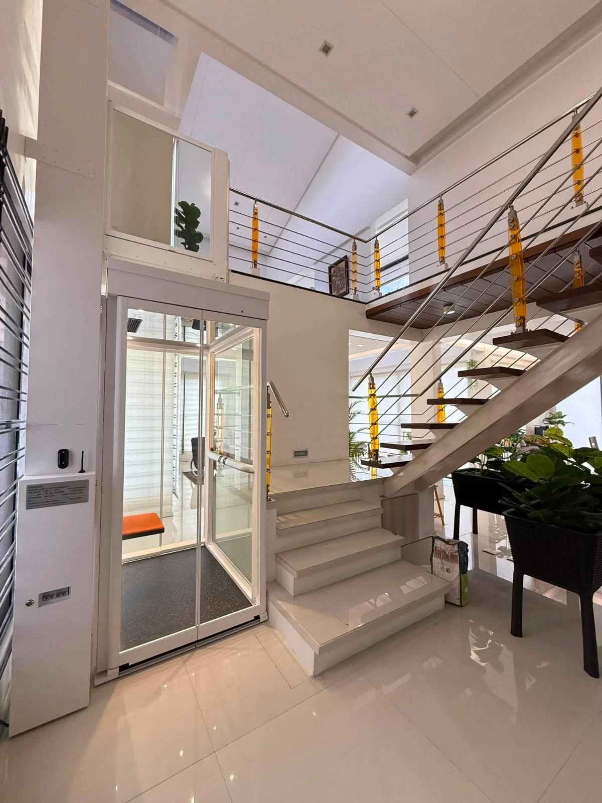 Service Lift Rumah Ascenda 2026: Biaya, Jadwal, dan Checklist Teknisi 5 Lift rumah Ascenda Size XL di samping tangga dengan pintu lantai bawah terbuka