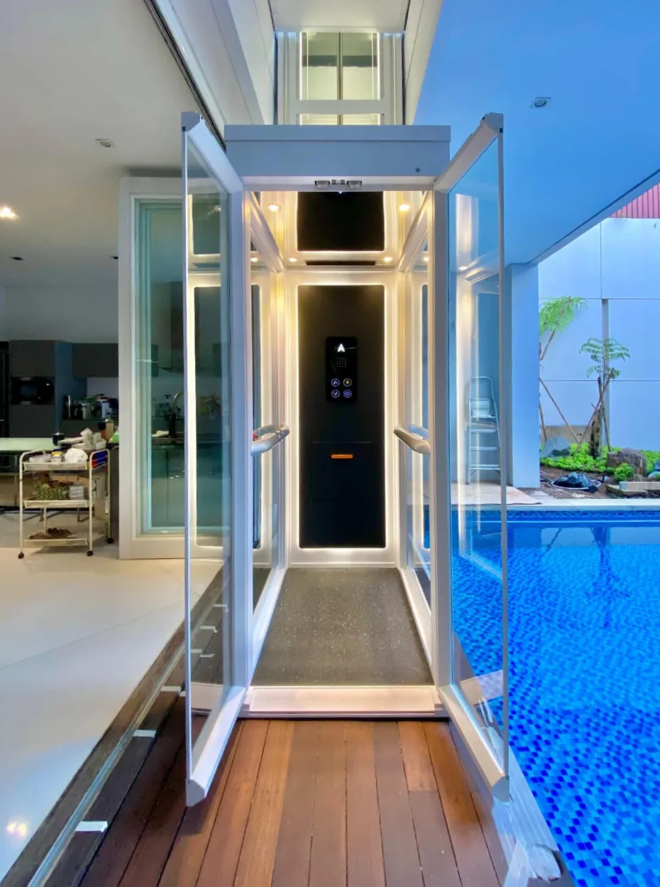 Tampak samping lift rumah Ascenda dengan shaft kaca yang terpasang di samping kolam renang dan area teras.