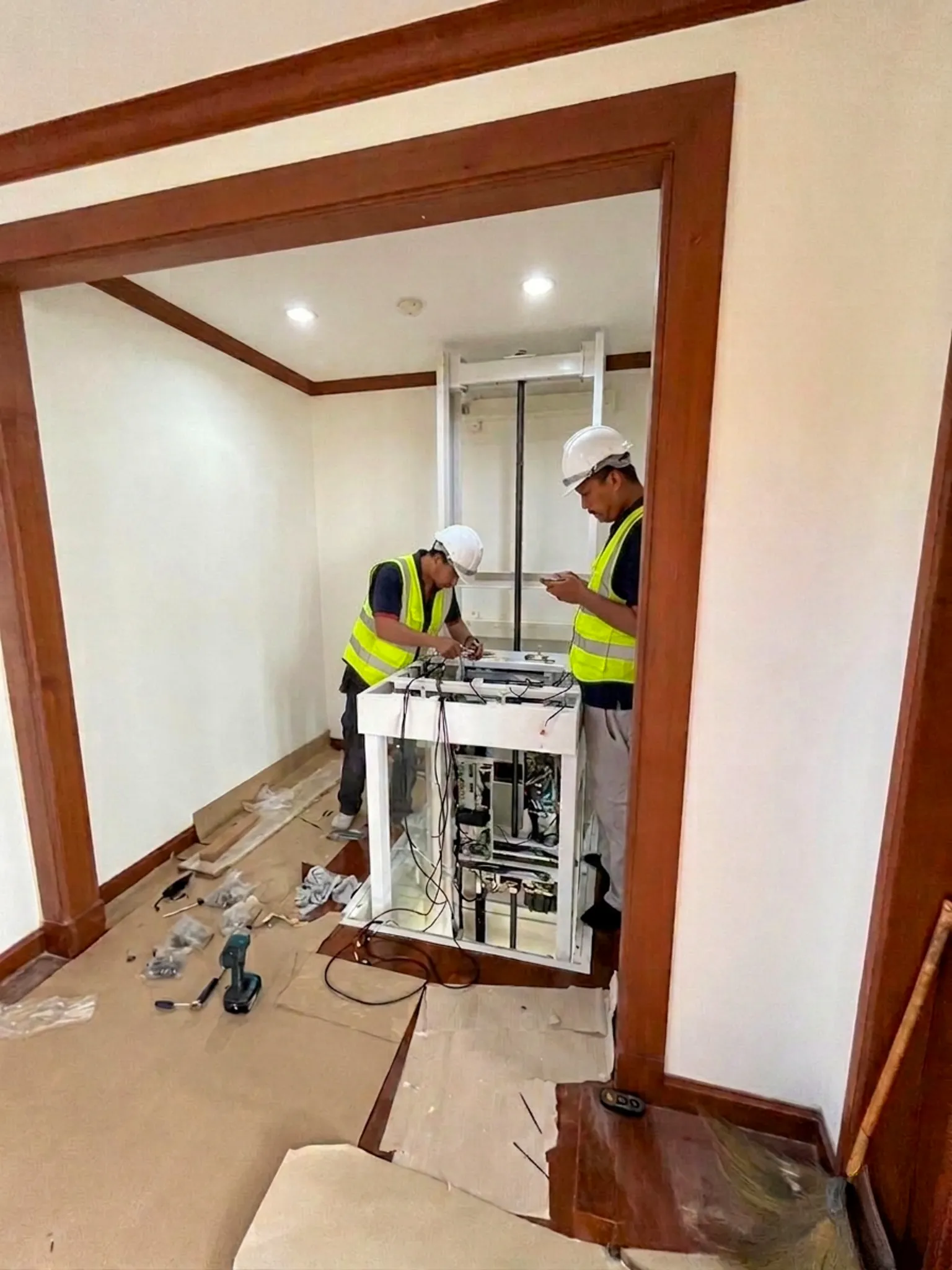 Dua teknisi Ascenda by Cibes melakukan instalasi dan pengecekan lift rumah di area interior rumah.